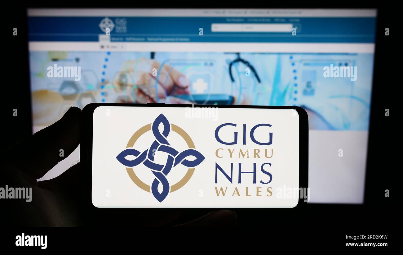 Persona che detiene lo smartphone con il logo del sistema sanitario britannico NHS Galles sullo schermo di fronte al sito Web. Concentrarsi sul display del telefono. Foto Stock