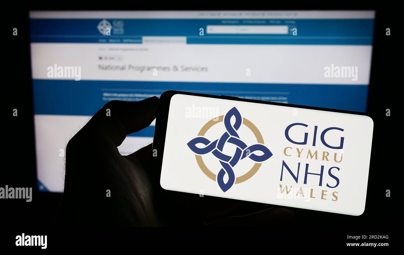 Persona che tiene il cellulare con il logo del sistema sanitario britannico NHS Galles sullo schermo di fronte alla pagina web. Concentrarsi sul display del telefono. Foto Stock