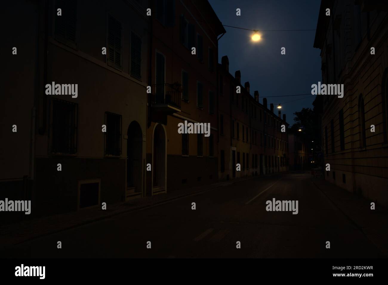 Strada stretta con una lampada a sospensione sopra di essa in una città italiana al crepuscolo Foto Stock