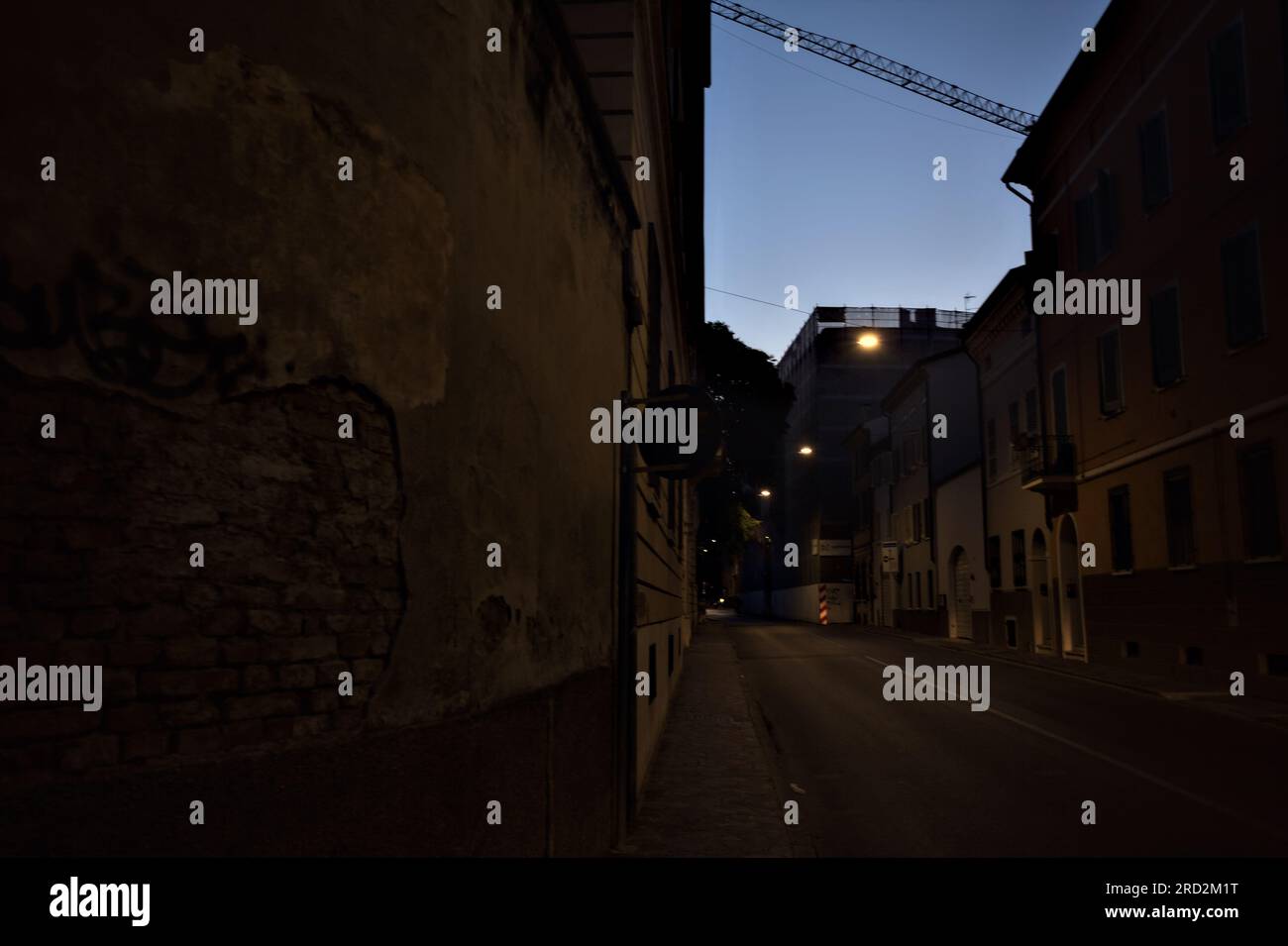 Strada stretta con una lampada a sospensione sopra di essa in una città italiana al crepuscolo Foto Stock