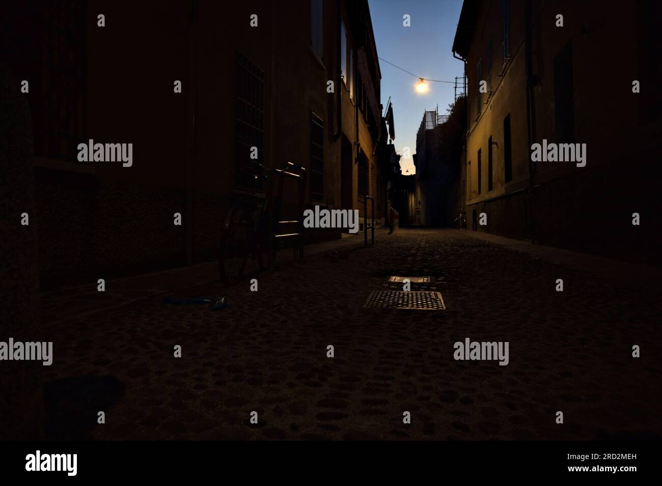 Strada stretta con una lampada a sospensione sopra di essa in una città italiana al crepuscolo Foto Stock