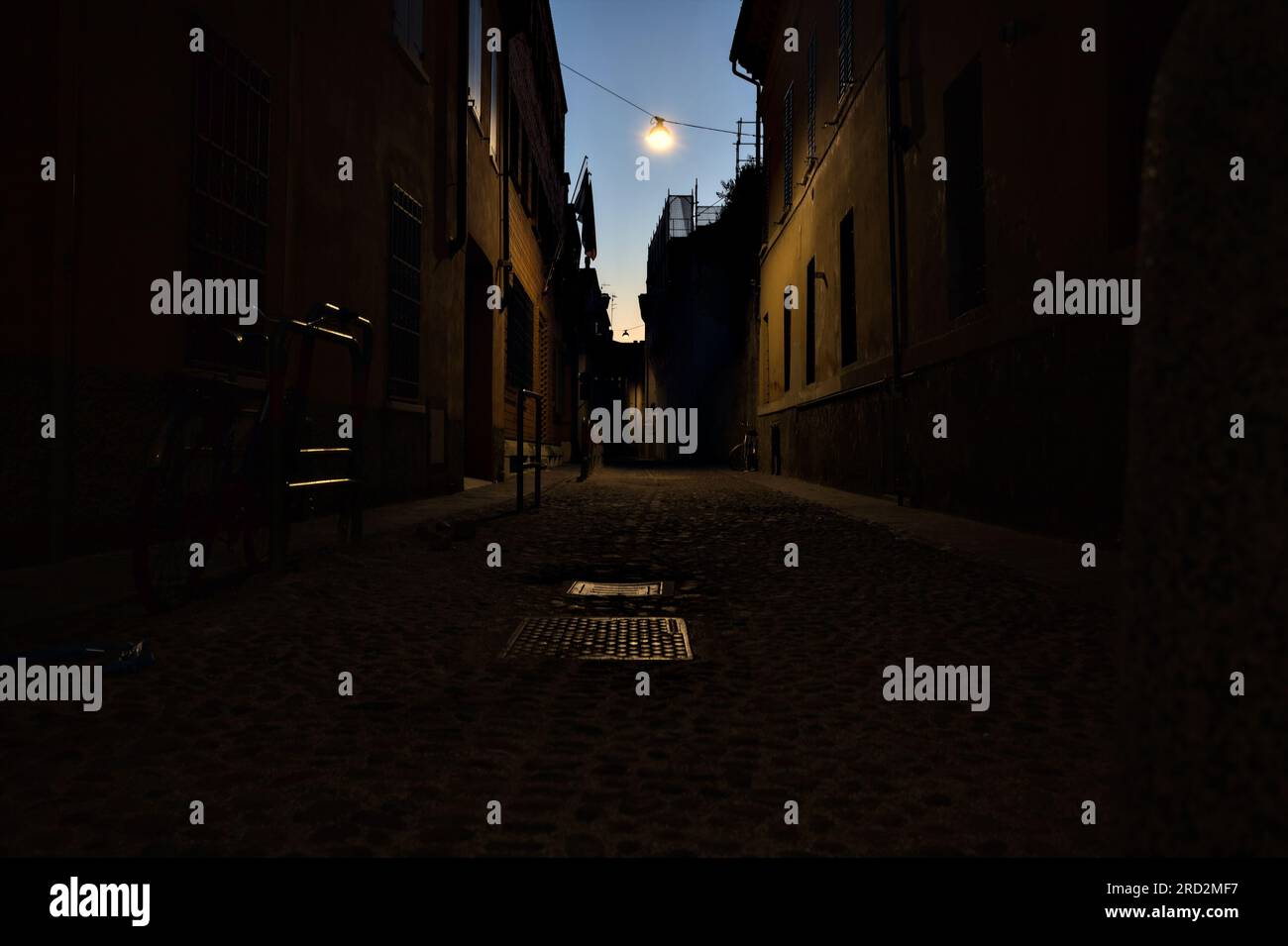 Strada stretta con una lampada a sospensione sopra di essa in una città italiana al crepuscolo Foto Stock