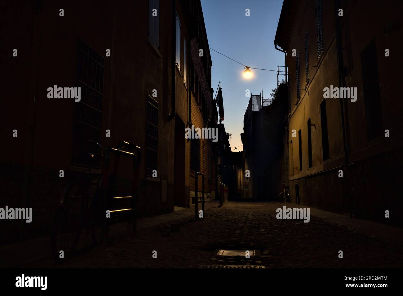 Strada stretta con una lampada a sospensione sopra di essa in una città italiana al crepuscolo Foto Stock