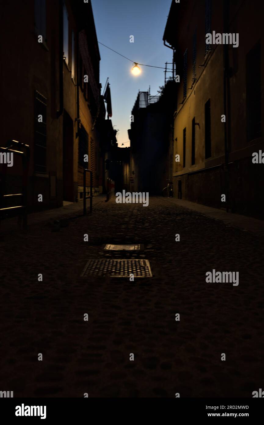 Strada stretta con una lampada a sospensione sopra di essa in una città italiana al crepuscolo Foto Stock