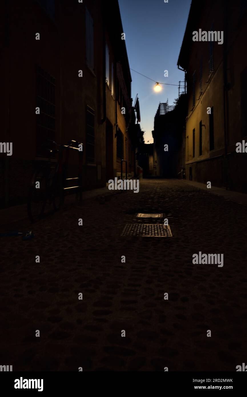 Strada stretta con una lampada a sospensione sopra di essa in una città italiana al crepuscolo Foto Stock