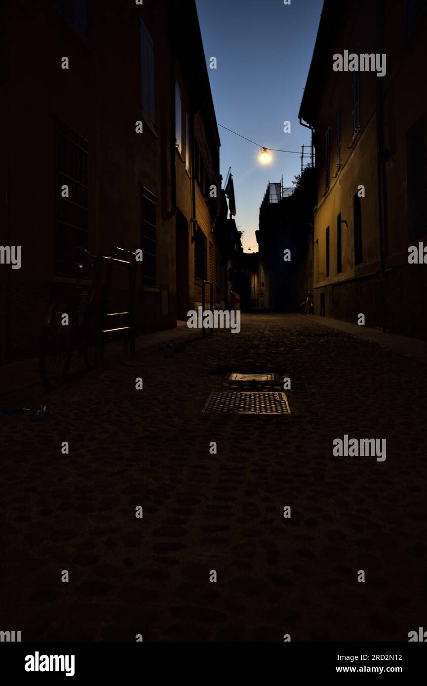 Strada stretta con una lampada a sospensione sopra di essa in una città italiana al crepuscolo Foto Stock