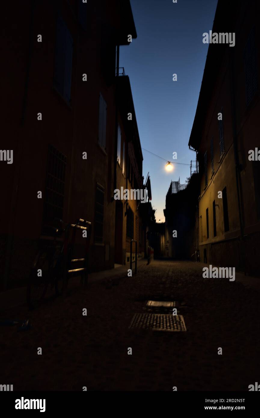 Strada stretta con una lampada a sospensione sopra di essa in una città italiana al crepuscolo Foto Stock