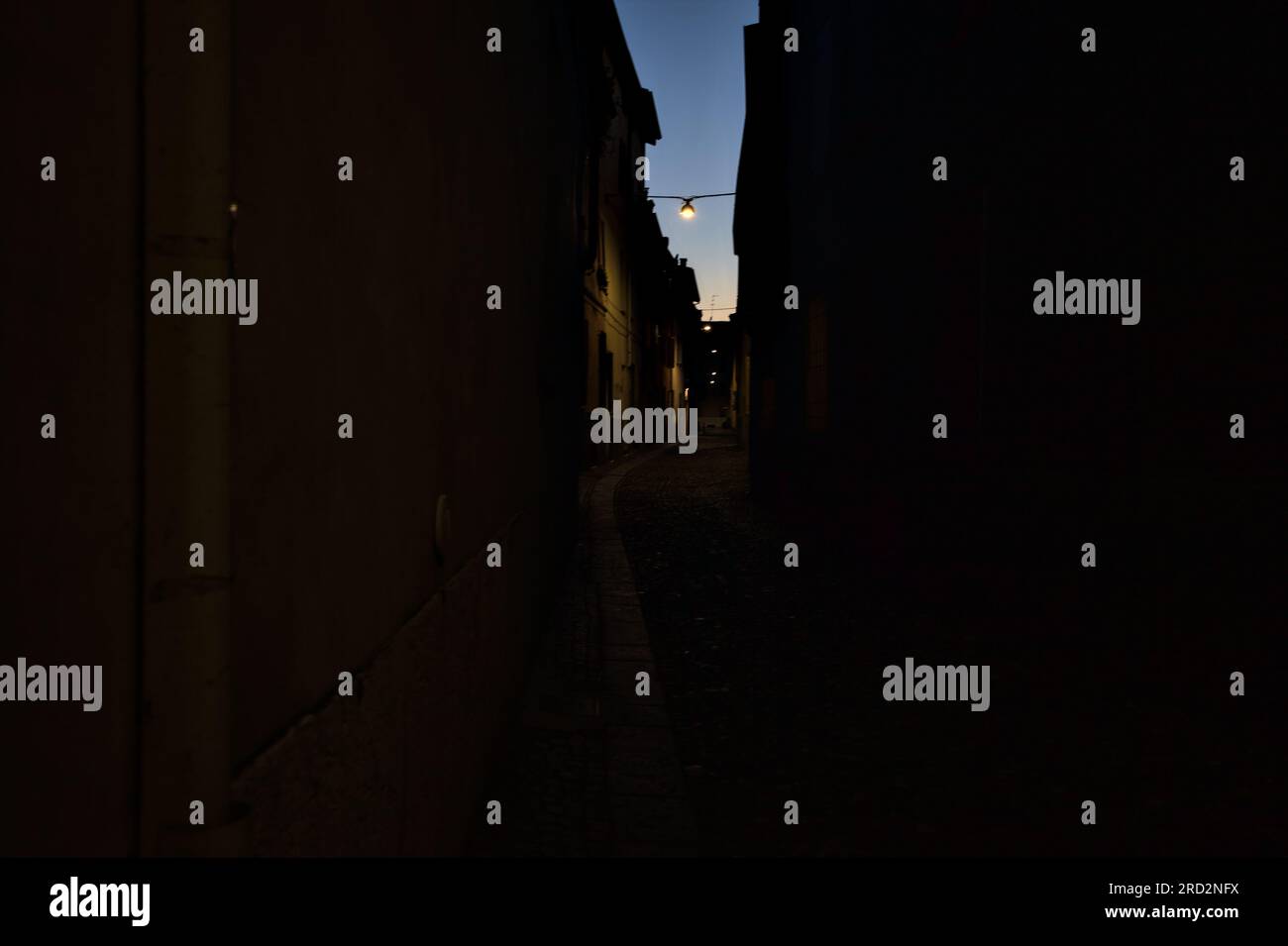 Strada stretta con una lampada a sospensione sopra di essa in una città italiana al crepuscolo Foto Stock