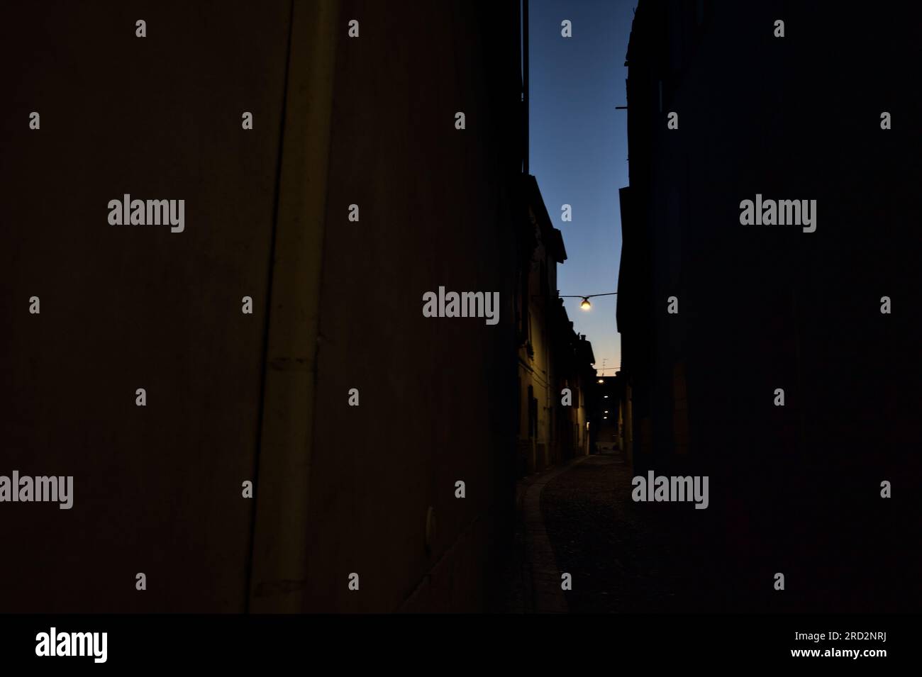 Strada stretta con una lampada a sospensione sopra di essa in una città italiana al crepuscolo Foto Stock