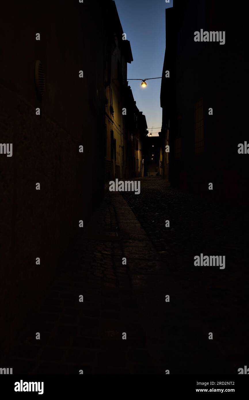 Strada stretta con una lampada a sospensione sopra di essa in una città italiana al crepuscolo Foto Stock