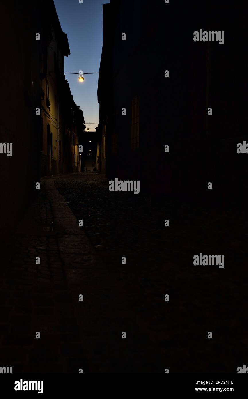 Strada stretta con una lampada a sospensione sopra di essa in una città italiana al crepuscolo Foto Stock