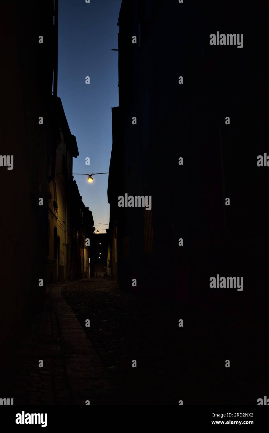 Strada stretta con una lampada a sospensione sopra di essa in una città italiana al crepuscolo Foto Stock