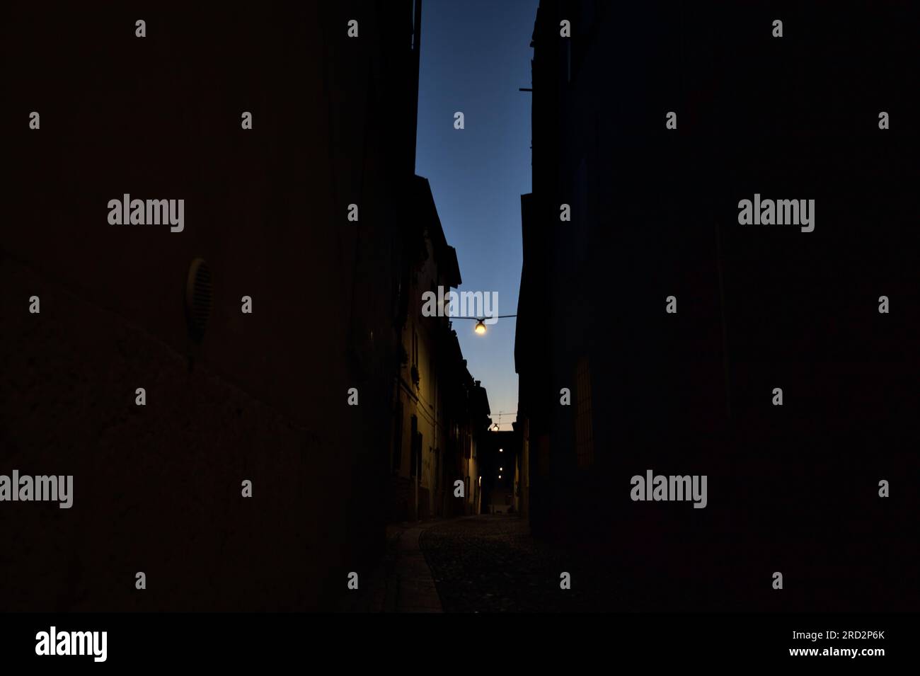 Strada stretta con una lampada a sospensione sopra di essa in una città italiana al crepuscolo Foto Stock