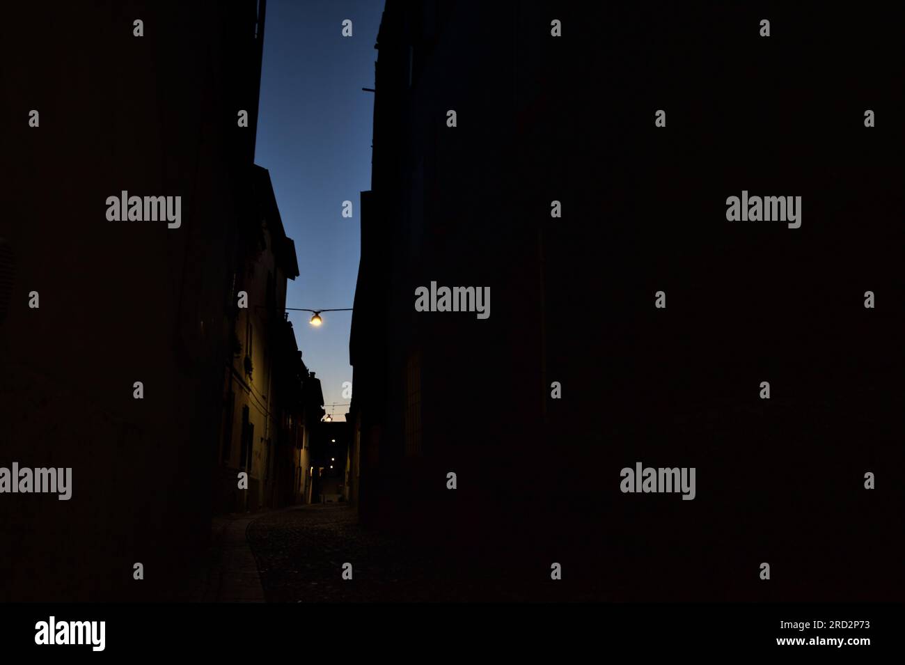Strada stretta con una lampada a sospensione sopra di essa in una città italiana al crepuscolo Foto Stock