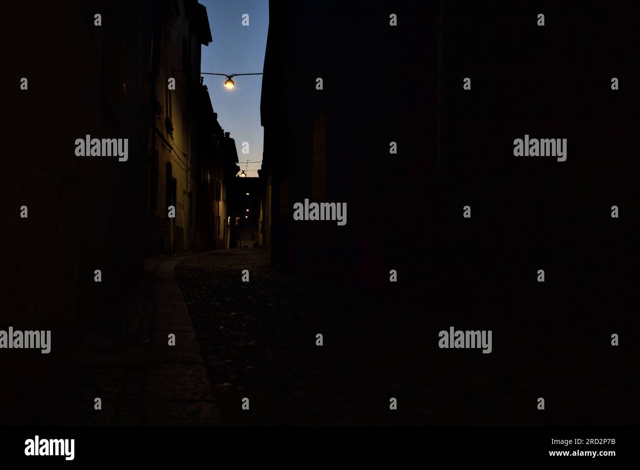 Strada stretta con una lampada a sospensione sopra di essa in una città italiana al crepuscolo Foto Stock