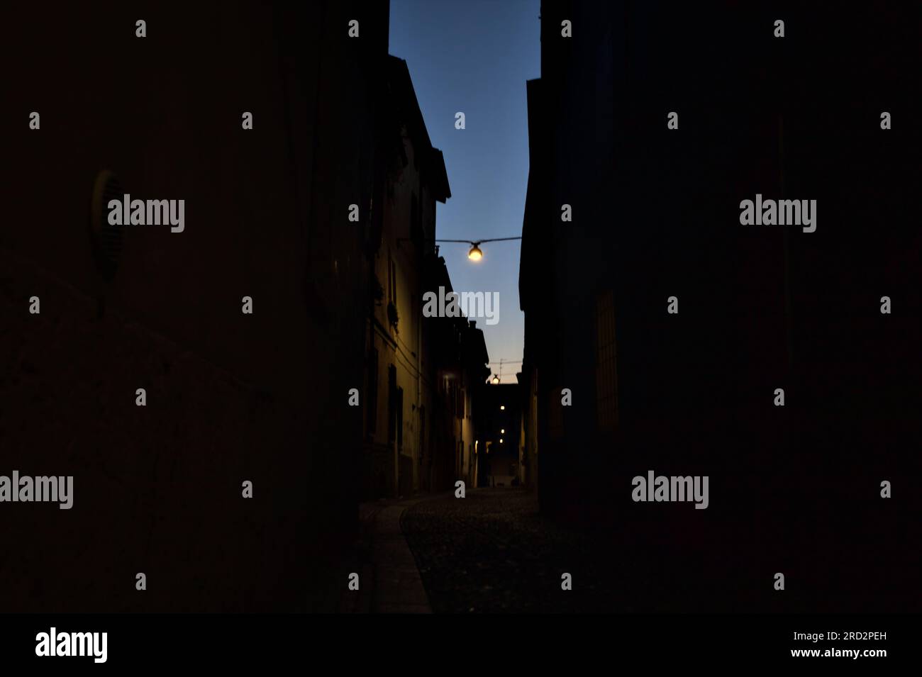 Strada stretta con una lampada a sospensione sopra di essa in una città italiana al crepuscolo Foto Stock