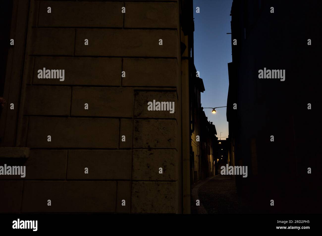 Strada stretta con una lampada a sospensione sopra di essa in una città italiana al crepuscolo Foto Stock
