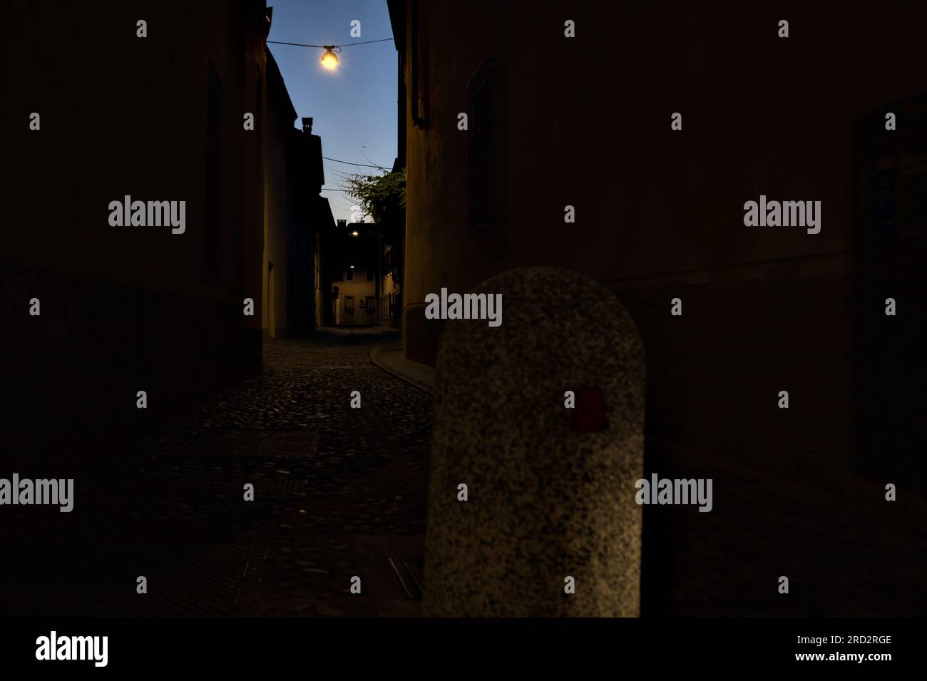 Strada stretta con una lampada a sospensione sopra di essa in una città italiana al crepuscolo Foto Stock