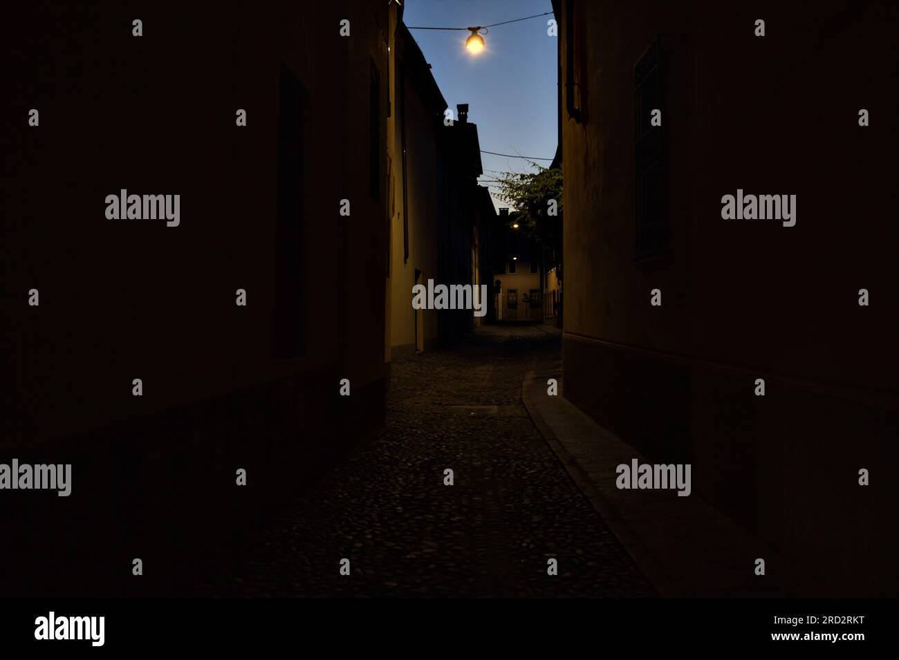 Strada stretta con una lampada a sospensione sopra di essa in una città italiana al crepuscolo Foto Stock