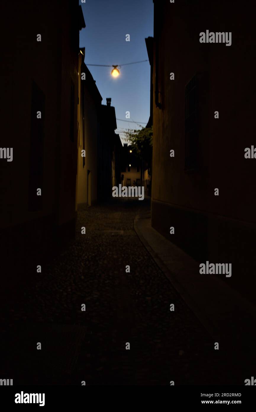 Strada stretta con una lampada a sospensione sopra di essa in una città italiana al crepuscolo Foto Stock