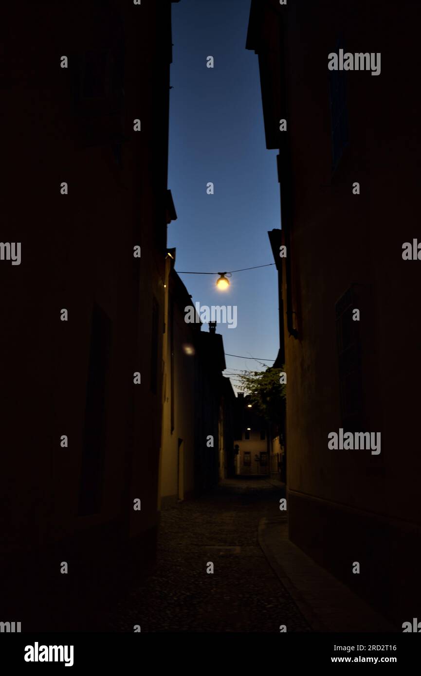 Strada stretta con una lampada a sospensione sopra di essa in una città italiana al crepuscolo Foto Stock