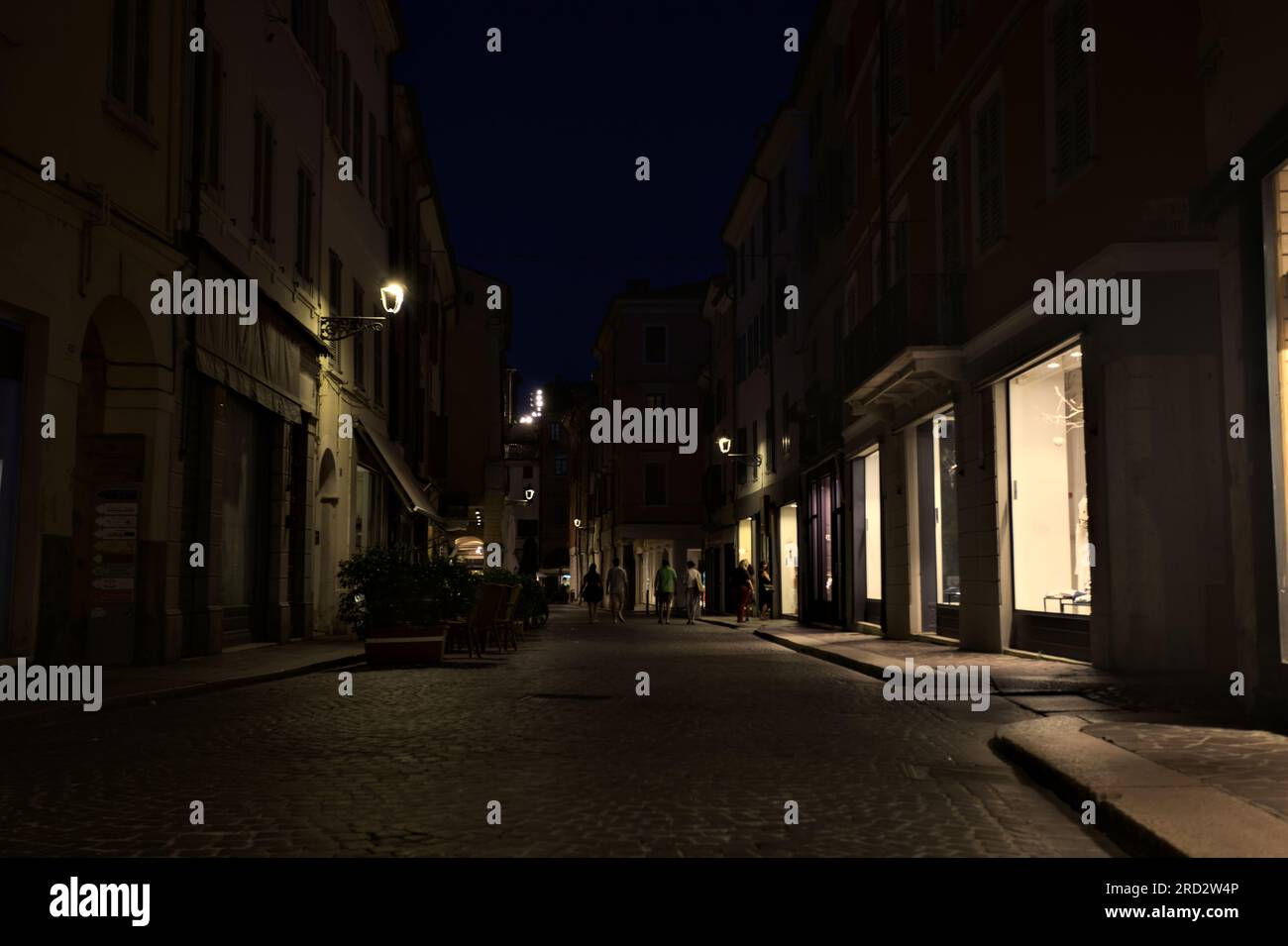 Strada acciottolata con vetrine di negozi e tavoli di ristoranti in una città italiana di notte Foto Stock