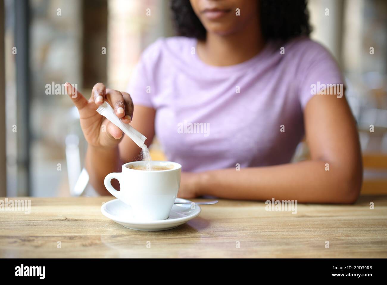 Primo piano di una donna nera che lancia zucchero in una tazza di caffè in una terrazza del bar Foto Stock