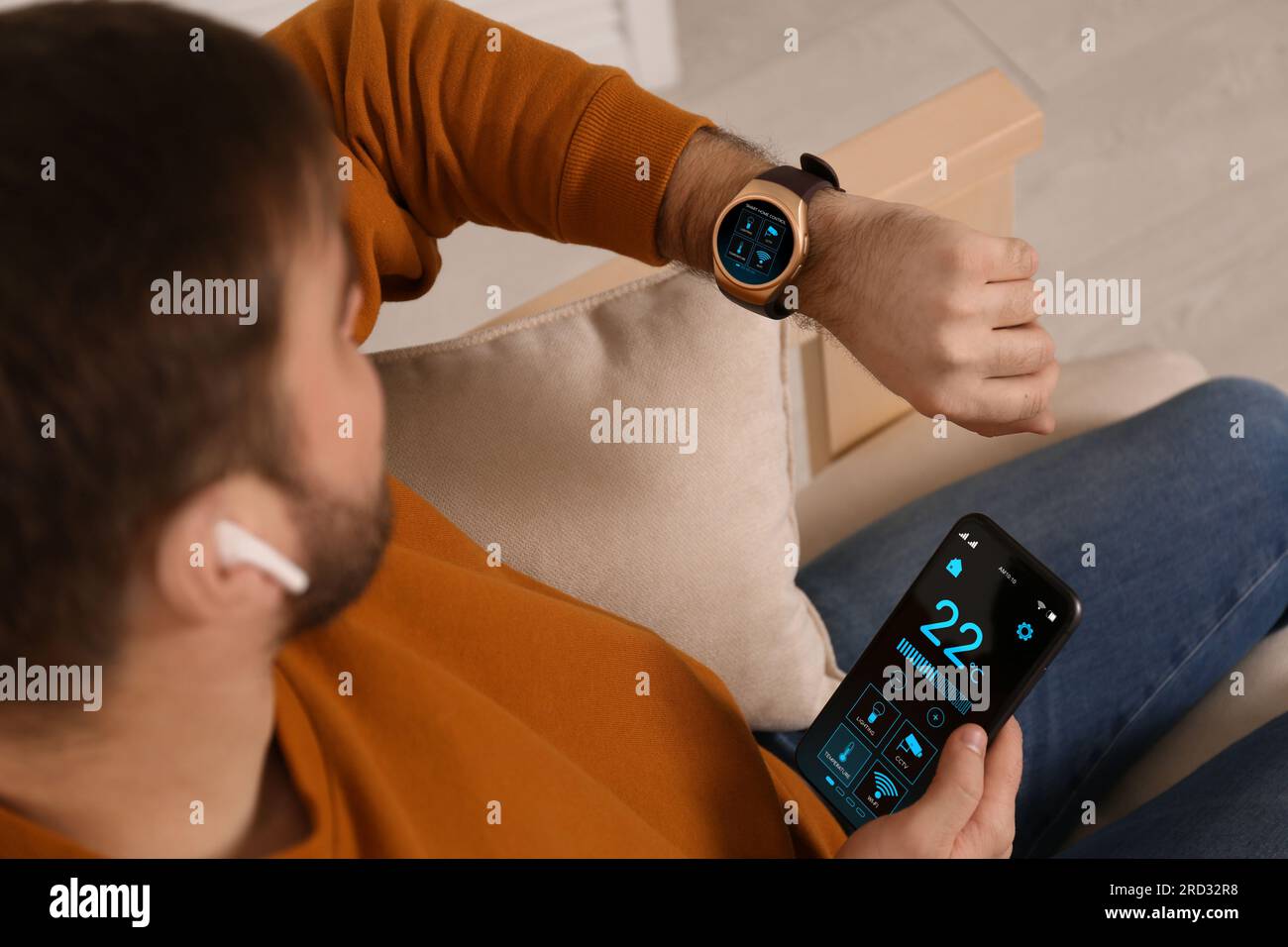 Sistema di controllo Smart Home da uomo tramite smartwatch e telefono cellulare in interni. Interfaccia app con icone sul display Foto Stock