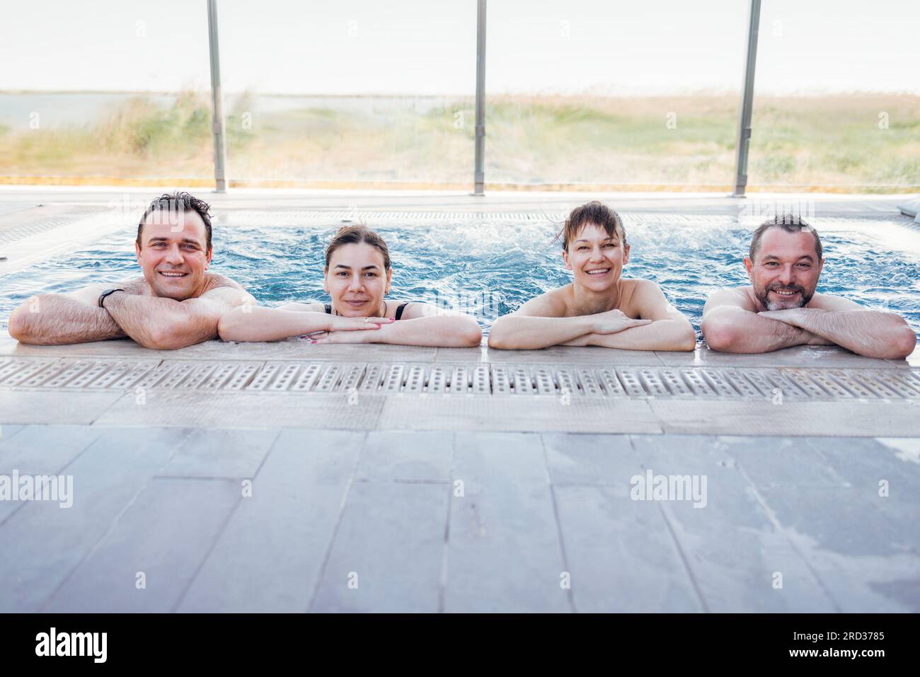 Due coppie sposate chiacchierano e fanno una piscina all'aperto. Gli amici ridono e si rilassano nell'acqua vorticosa. I giovani si rilassano in un centro benessere o in un hotel. Foto Stock