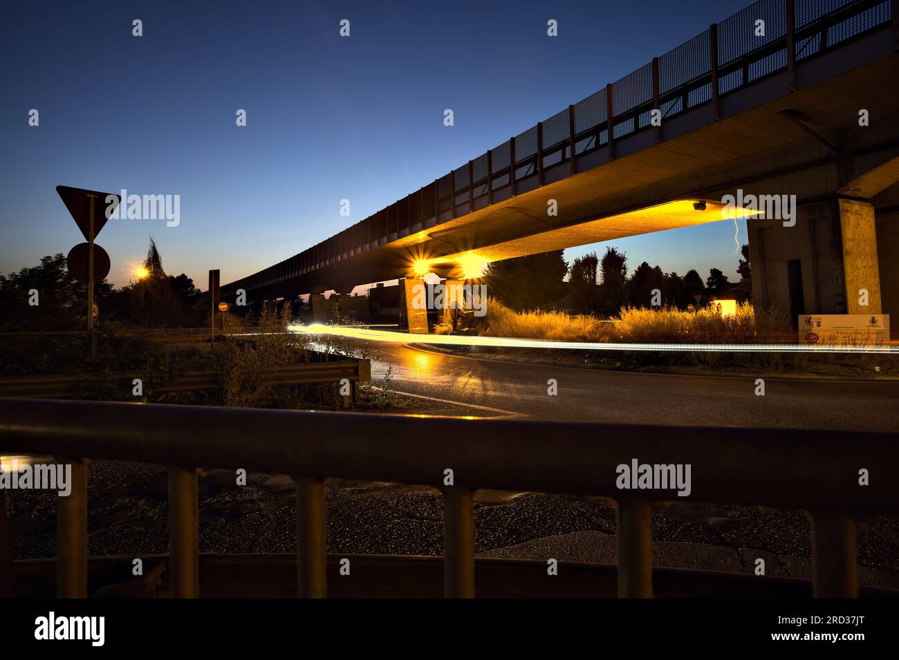 Rotatoria sotto un viadotto nella campagna italiana di notte vista da un marciapiede ai margini di una strada Foto Stock
