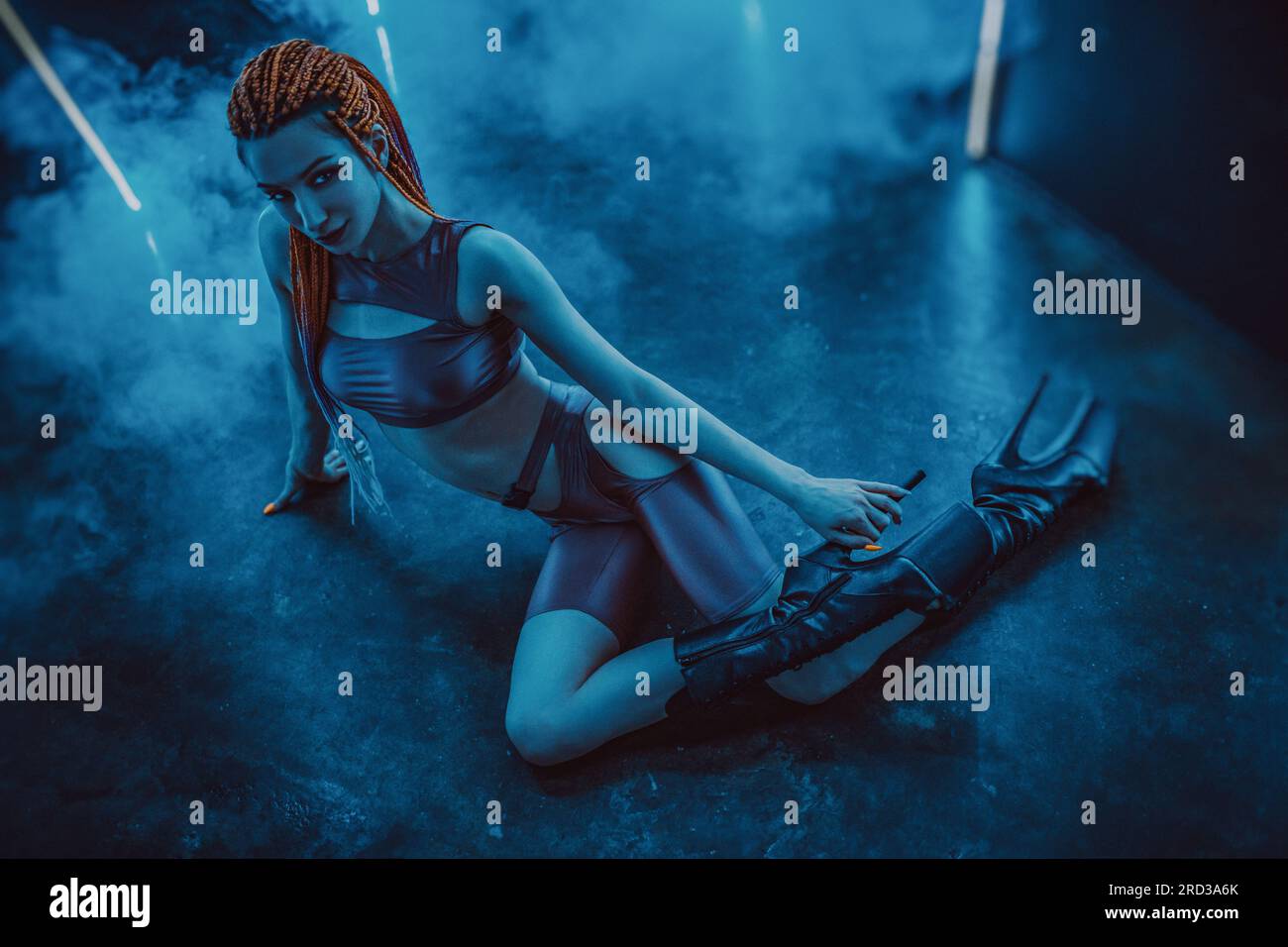 Giovane ballerina in posa nell'interno di un night club buio con luci blu e fumo Foto Stock