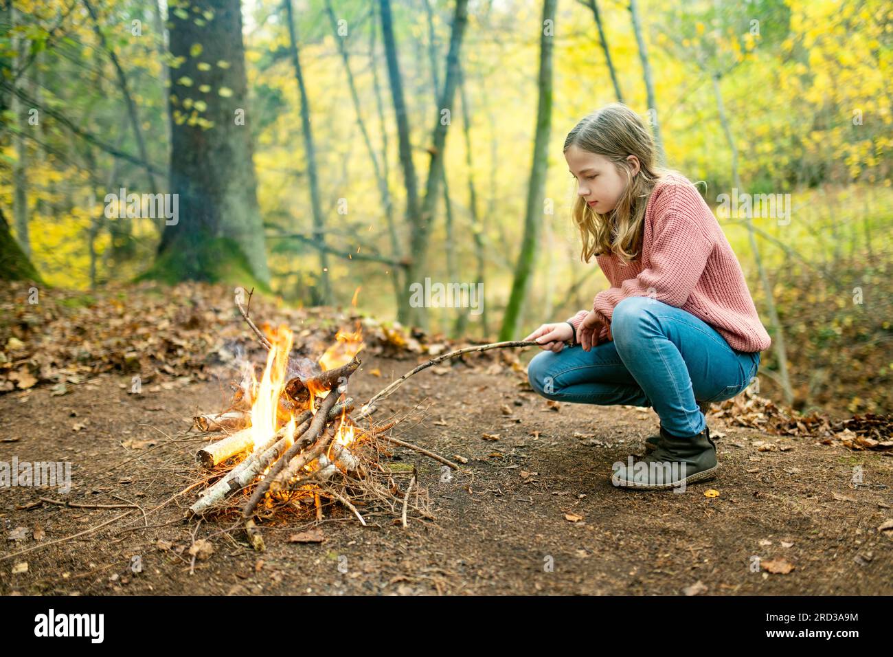 Carina ragazza preteen tostatura di marshmallows sul bastone a falò. Bambino divertirsi al campo di fuoco. Il campeggio con i bambini nella foresta di caduta. Vacanza in famiglia con Foto Stock