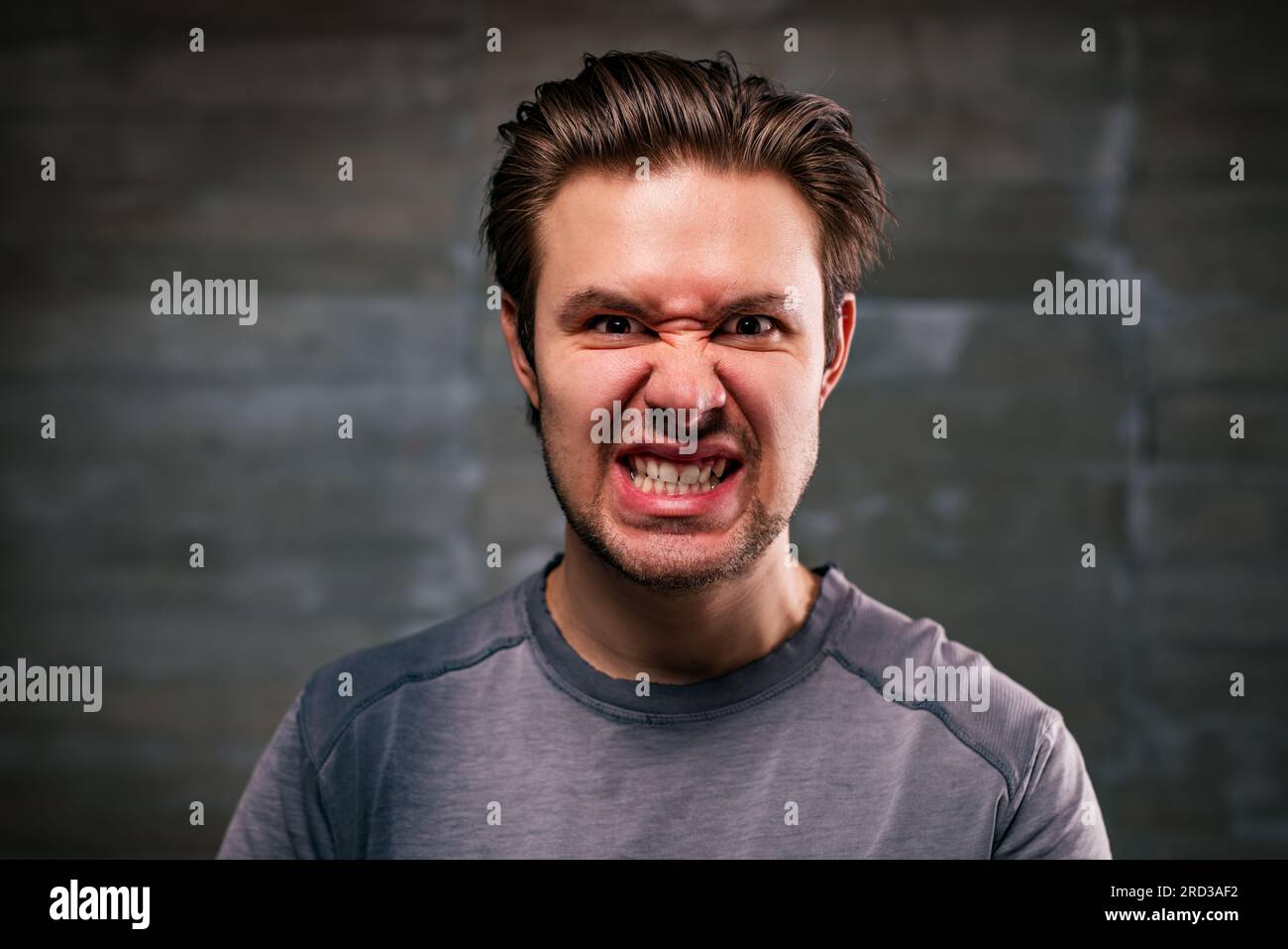 Ritratto arrabbiato di un giovane uomo su sfondo grigio Foto Stock