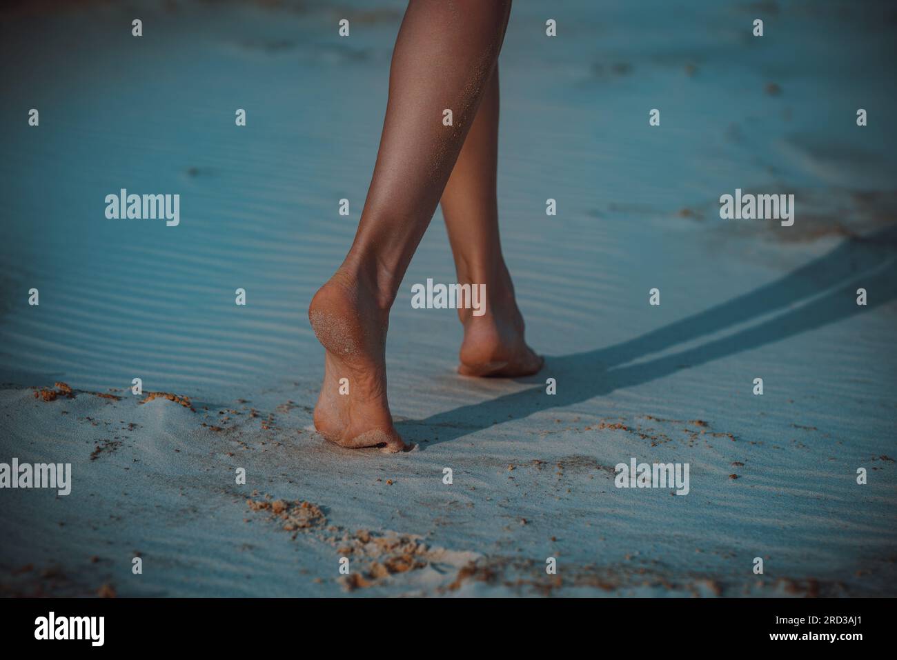 La giovane donna cammina a piedi scalzi sulla sabbia la sera Foto Stock