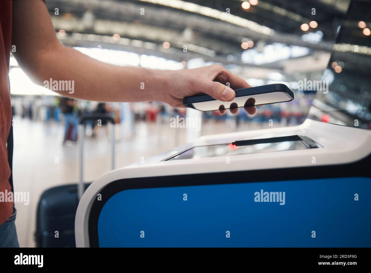 Mano dell'uomo durante l'uso della macchina di check-in self-service. Il passeggero esegue la scansione del biglietto sullo smartphone presso il terminal dell'aeroporto. Foto Stock