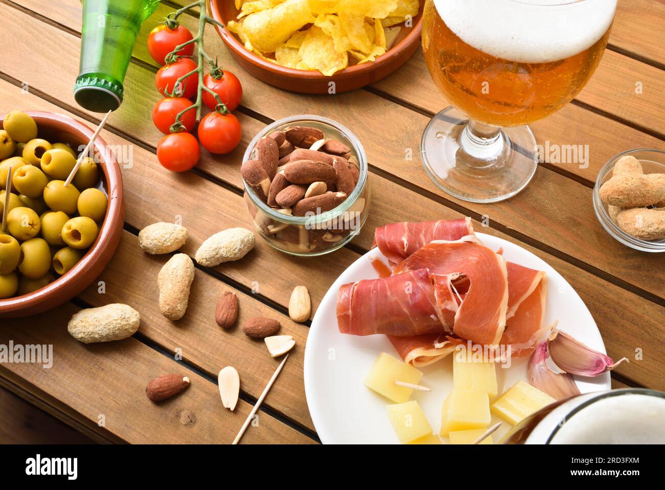 Spuntini preparati su un tavolo di legno e un bicchiere di birra con prosciutto stagionato, formaggio, olive, mandorle e arachidi e altri spuntini vari. Vista elevata. Foto Stock