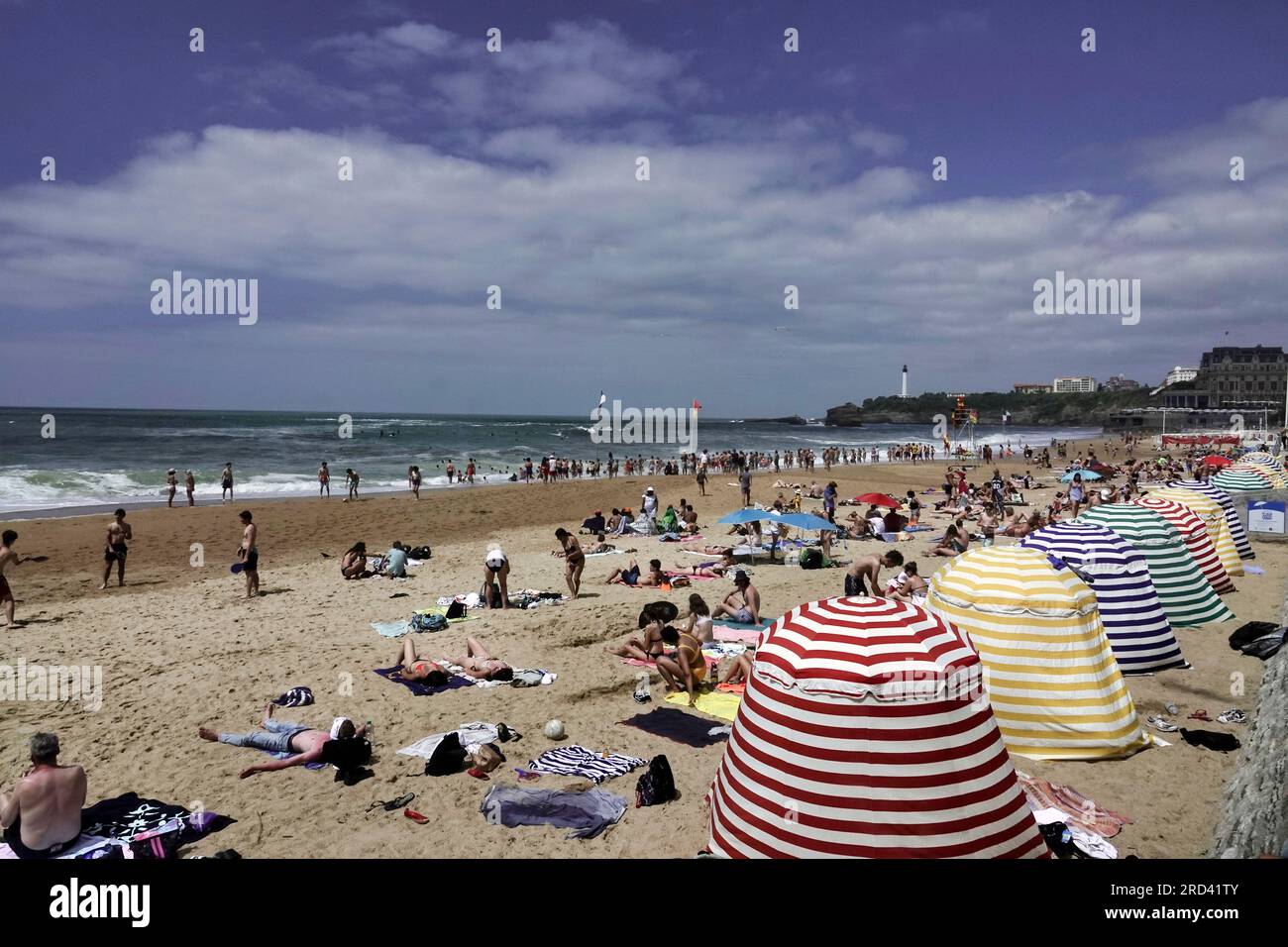 Biarritz, Francia, luglio 2023 Ó la grande PlageÓ Beach, Biarritz - con le colorate tende da spiaggia e vista sul faro di le Phare e sul caldo Foto Stock