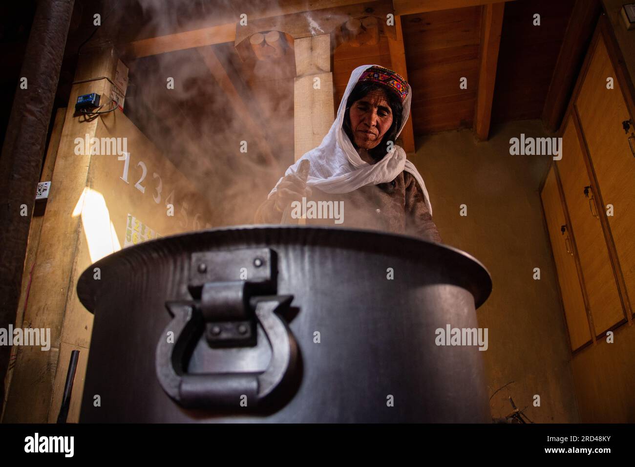 Una donna mescola una pentola di grano fermentato per 8 ore, rendendo seman prima del primo giorno di festa primaverile nella valle di Shimshal, nel nord del Pakistan. Foto Stock