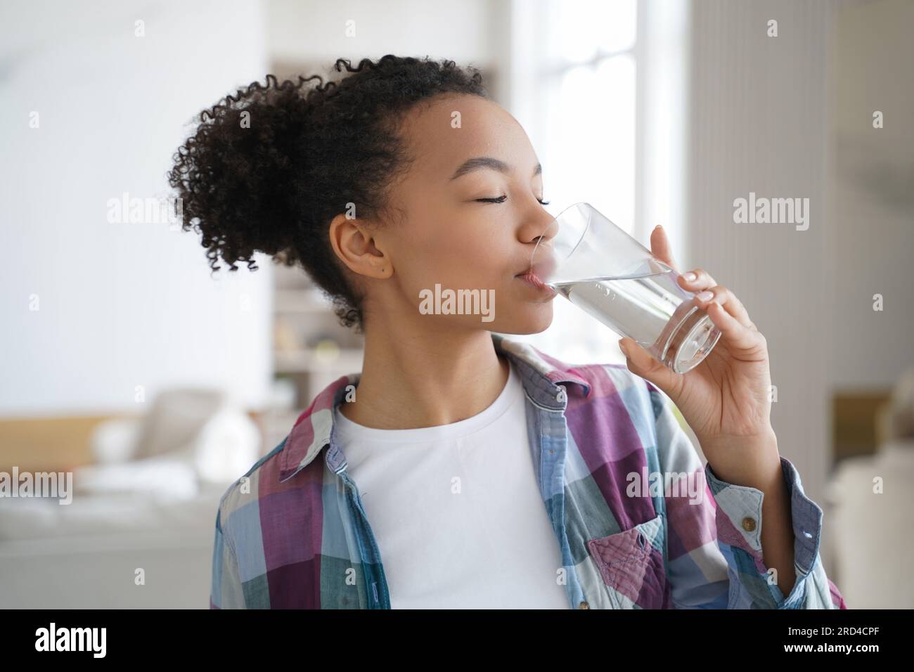 L'adolescente birazziale idrata con acqua filtrata, mantenendo la salute della pelle a casa. Foto Stock