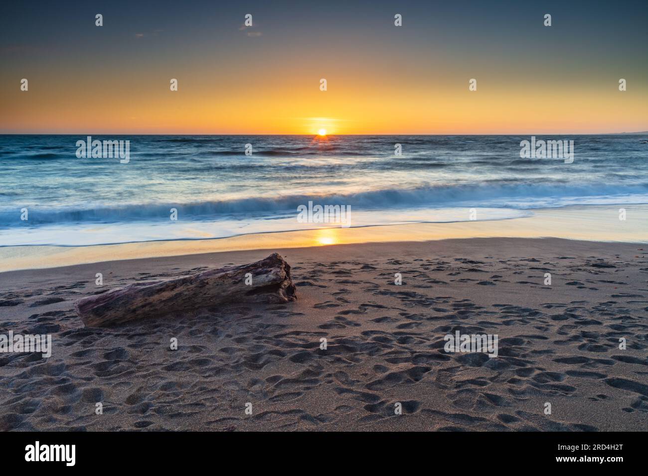 Moonstone Beach al tramonto a Cambria, California. Accedi alla spiaggia vuota, sabbia ricoperta di impronte. Sole all'orizzonte, riflesso sulla sabbia bagnata. Foto Stock