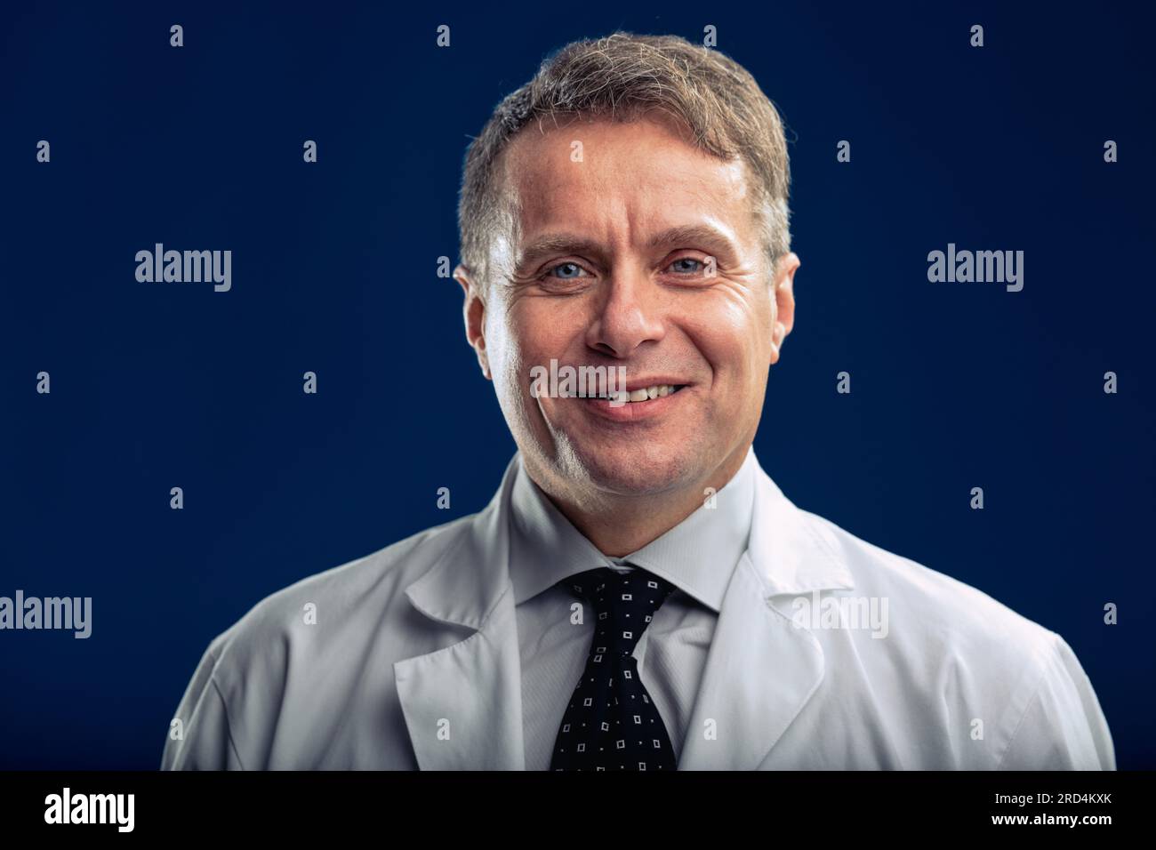 Ritratto in vita di uno scienziato che mostra un sorriso scomodo a una barzelletta disgustosa, chiudendo gli occhi con te. Di mezza età, sotto il suo cappotto da laboratorio, si indossa Foto Stock