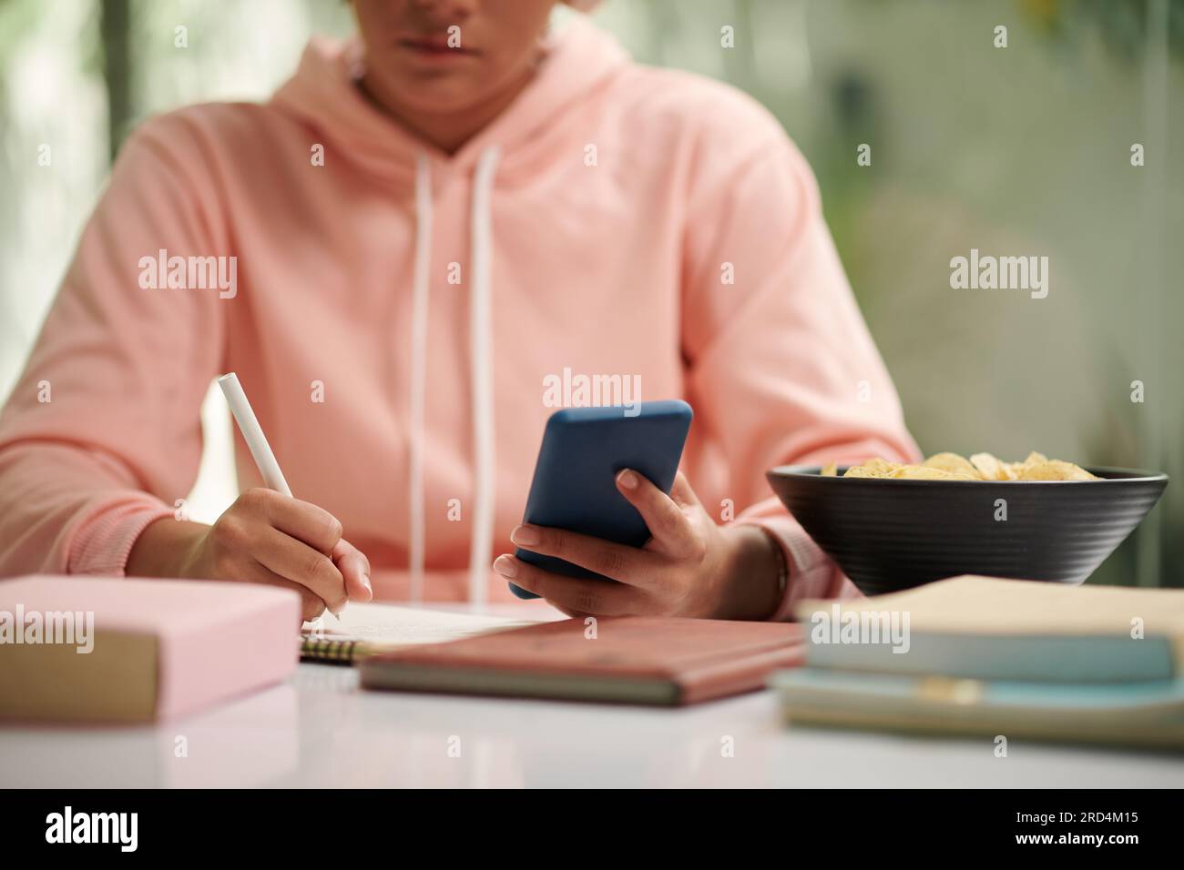 Immagine ritagliata di uno studente della scuola che controlla i messaggi di testo dal compagno di classe quando fa i compiti Foto Stock