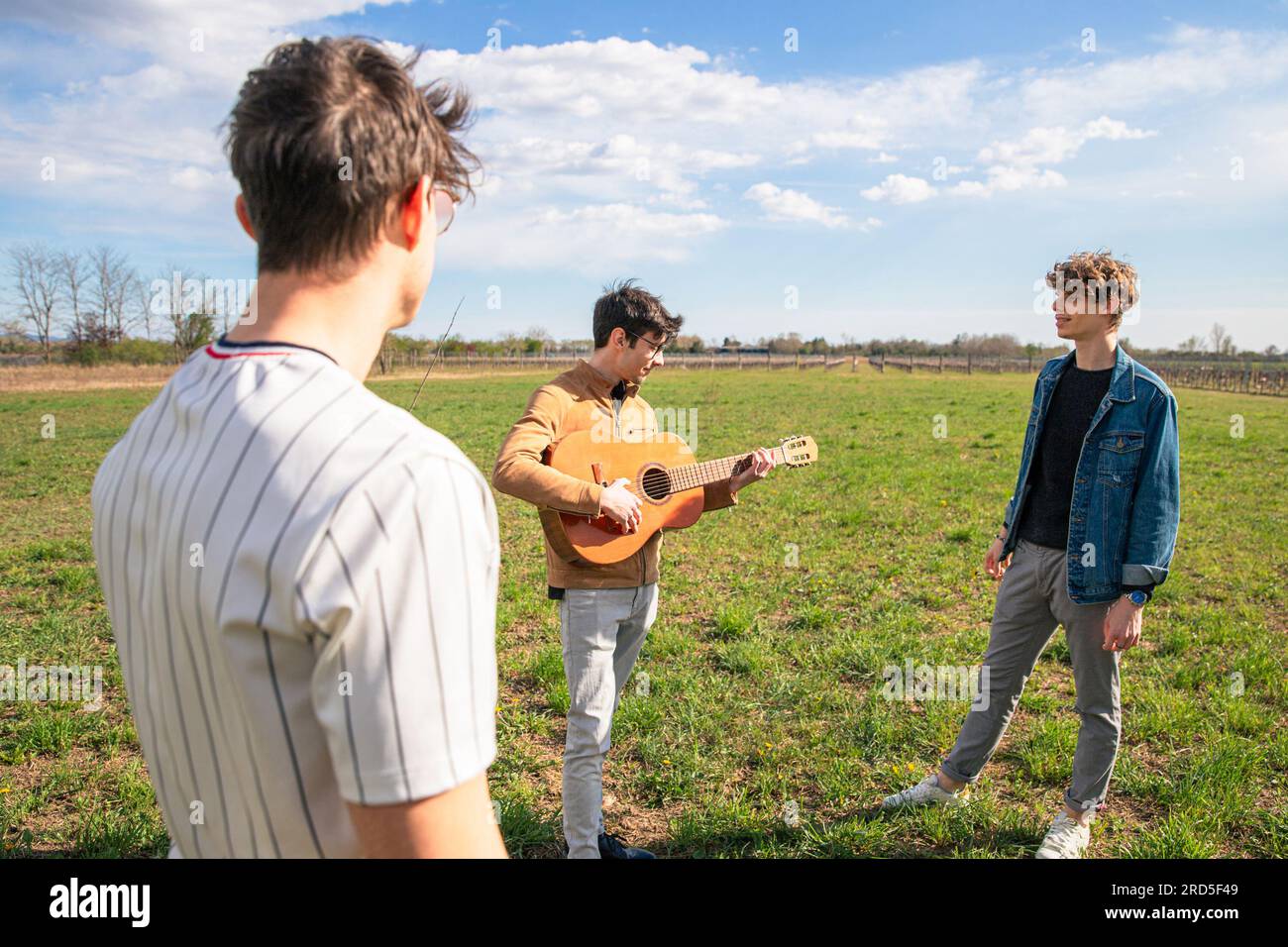 Un gruppo di amici si incontra in un campo per suonare la chitarra e cantare insieme Foto Stock