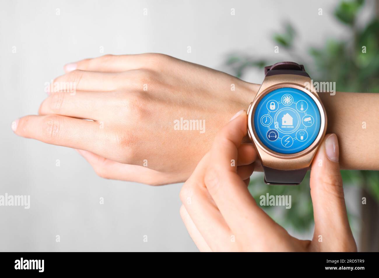Donna che imposta il sistema di controllo della casa intelligente tramite smartwatch al chiuso, primo piano. Interfaccia app con icone sul display Foto Stock