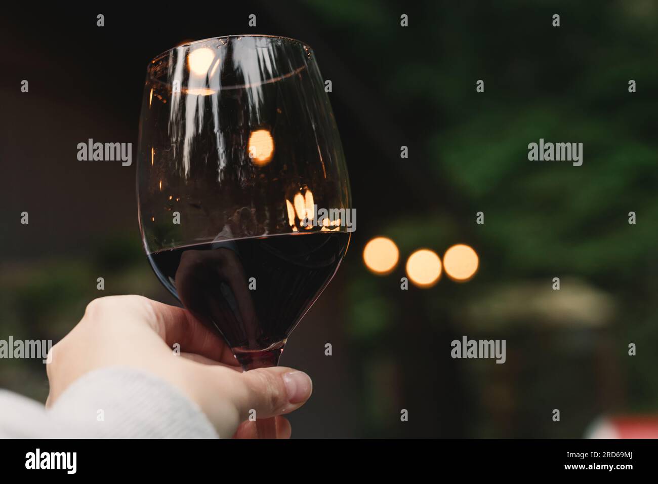 Donna che regge un bicchiere di rosso con luci sfocate sullo sfondo, rilassati sul patio e goditi la vita in cabina Foto Stock