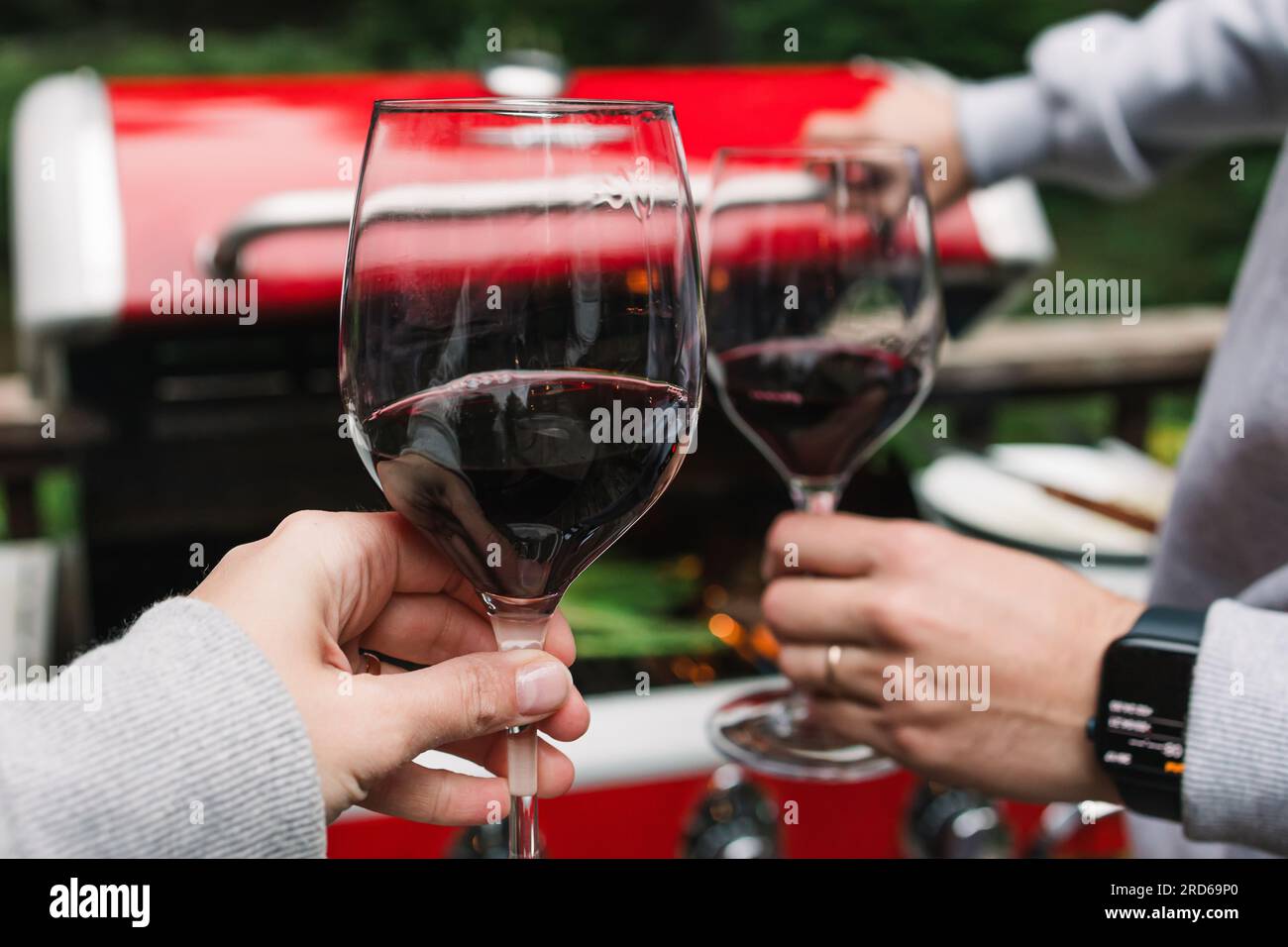 Uomo e donna che bevono vino rosso vicino alla griglia la sera d'estate, atmosfera accogliente Foto Stock