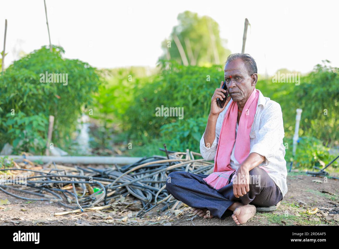 felice contadino seduto in terra a parlare al telefono , vecchio contadino indiano Foto Stock