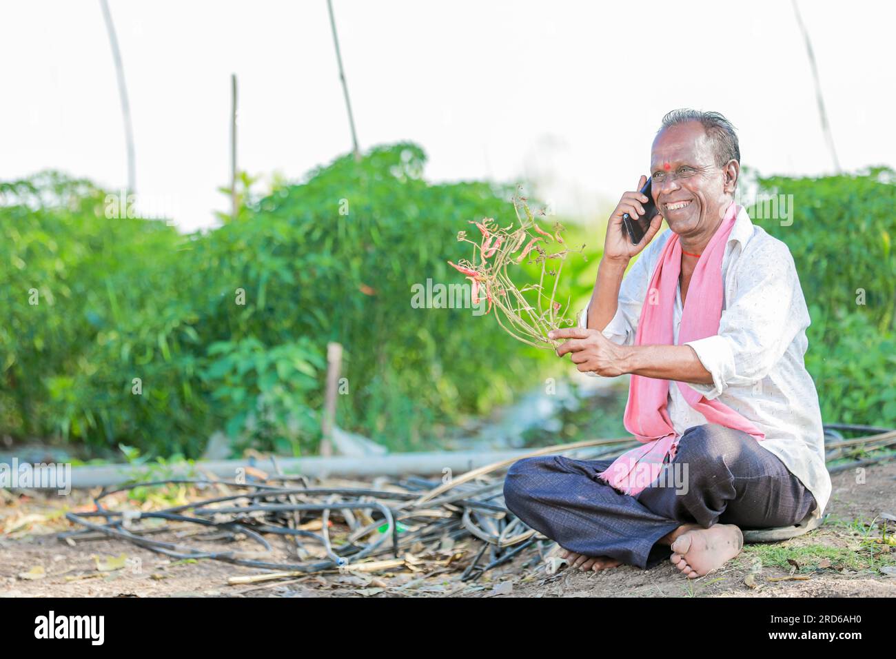 felice contadino seduto in terra a parlare al telefono , vecchio contadino indiano Foto Stock