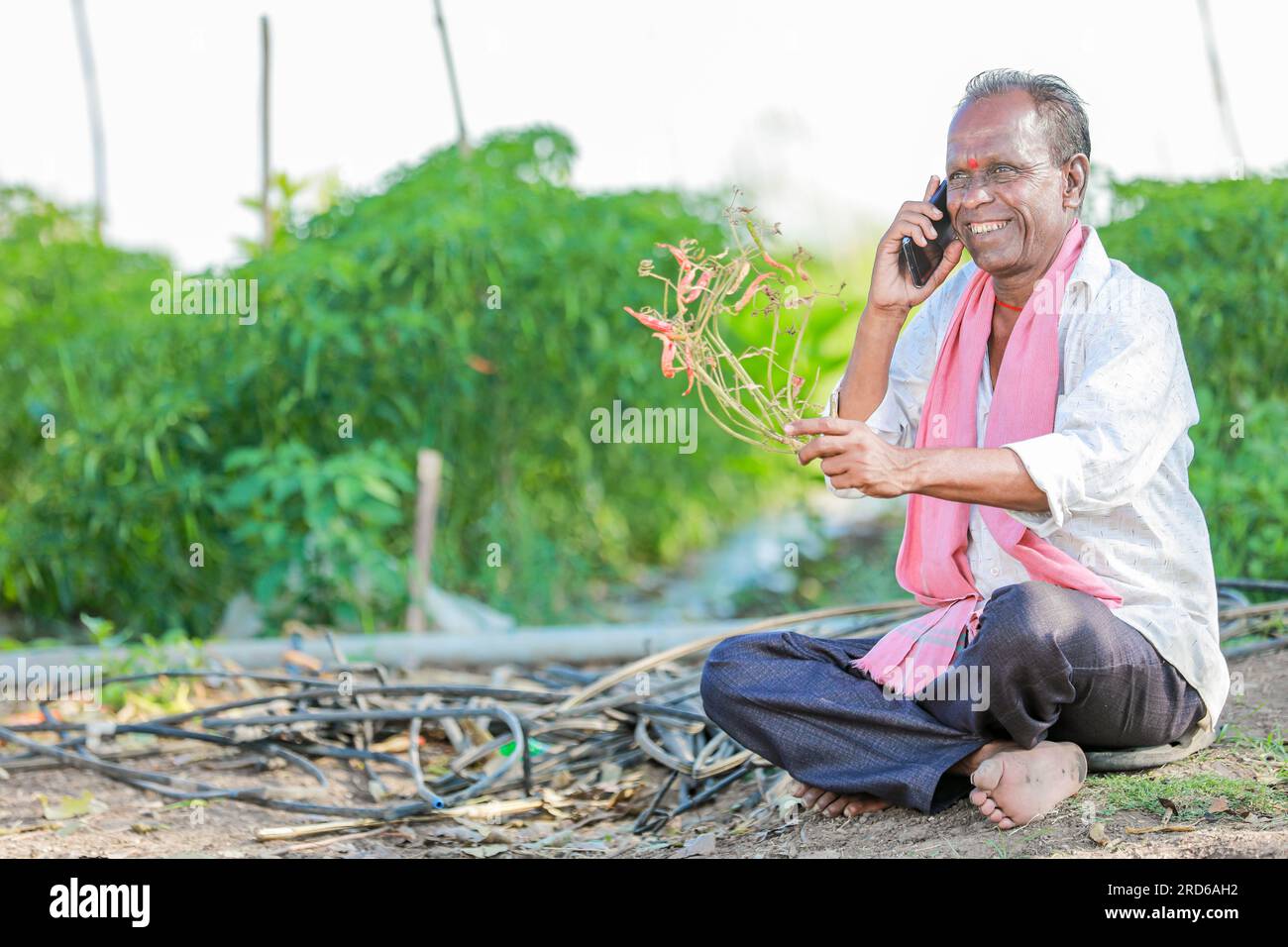 felice contadino seduto in terra a parlare al telefono , vecchio contadino indiano Foto Stock