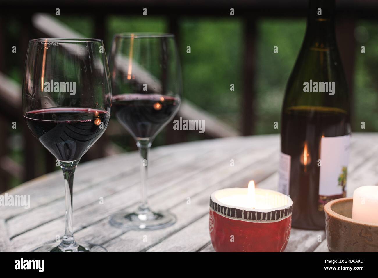 Due bicchieri con vino rosso in piedi sul tavolo di legno con candela a fuoco, atmosfera romantica Foto Stock